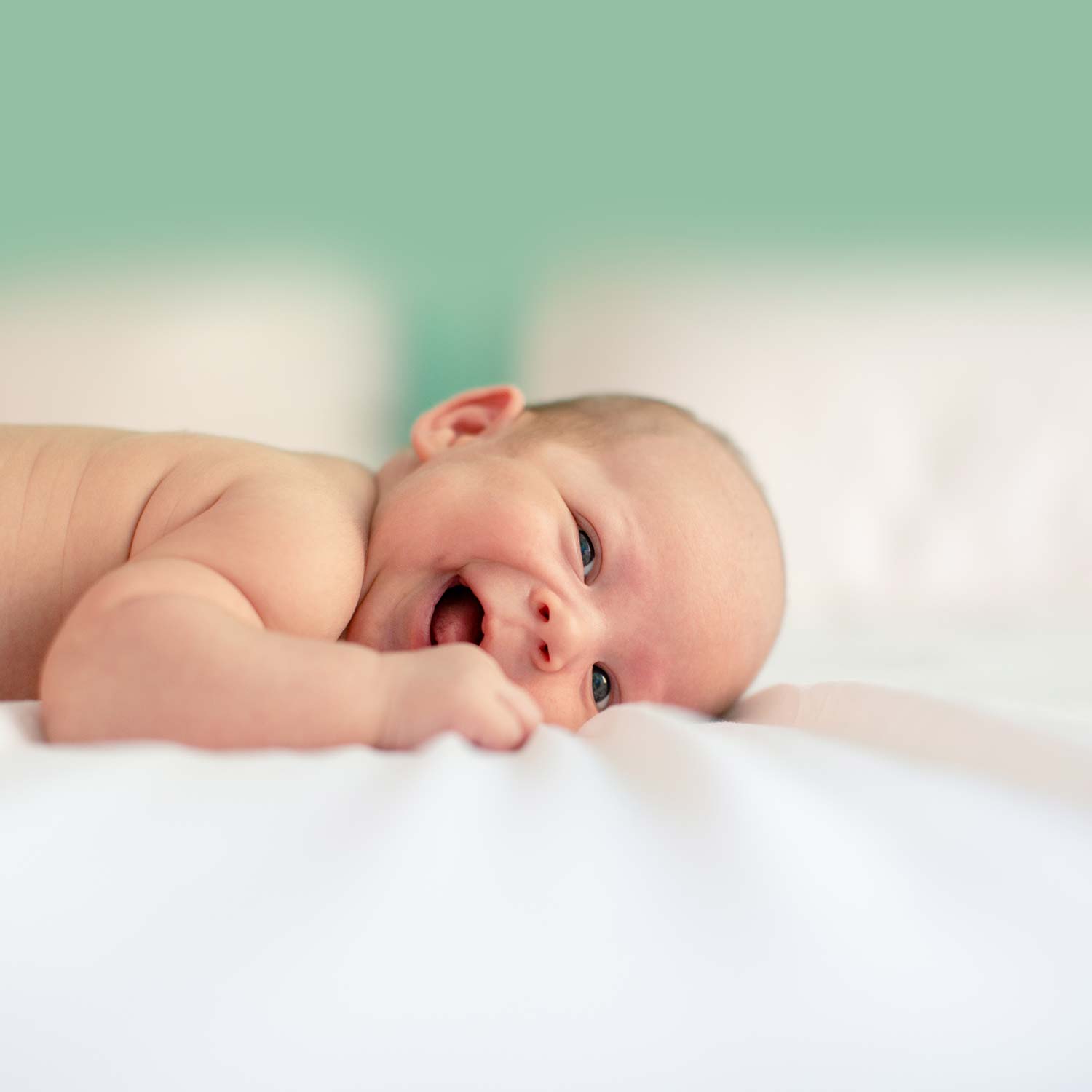 Happy baby that is laying on white bed sheets