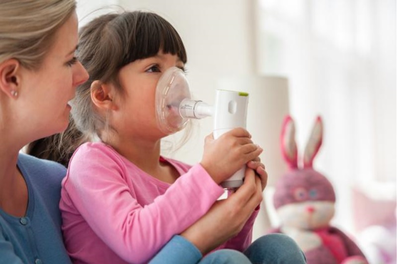 A mother helping a young girl use a nebulizer